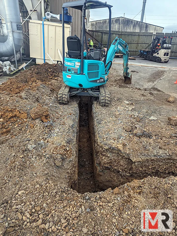 Mini digger trenching for underground power cable at an industrial site